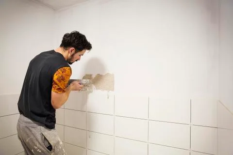 A builder, tiler placing white ceramic tiles on a wall in a bathroom. Stock Photos