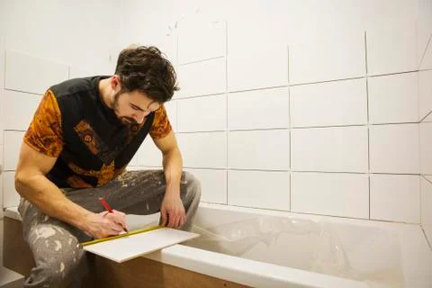 A builder, tiler working in a bathroom, marking a tile with a pencil. Stock Photos