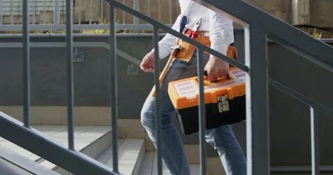 Builder with toolbox and tool-belt walks up stairs on working day Stockbeeldmateriaal 258504451