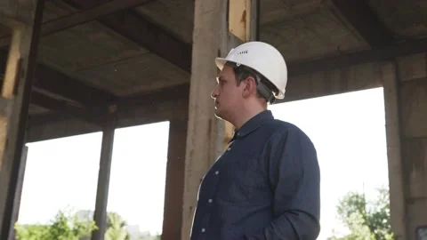 Builder turns to camera, puts on white mask, construction site in the background Stock Footage 138244148