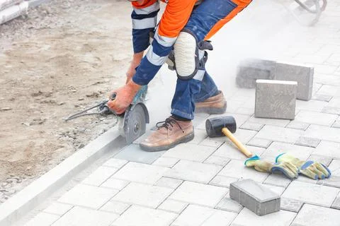 A builder uses a grinder and a diamond cutting disc to cut paving slabs in a  Stock Photos