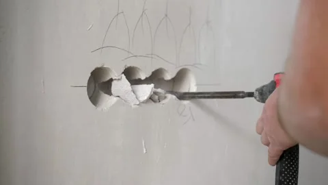 The builder uses a hammer drill to make round holes in the wall for installing Stock Footage 302285161