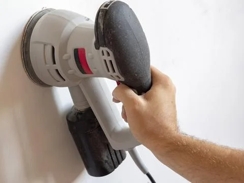 A Builder uses a sander to process a white concrete wall. Construction concer Stock Photos