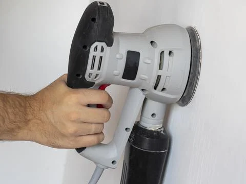 A Builder uses a sander to process a white concrete wall. Construction concer Stock Photos