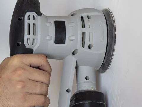 A Builder uses a sander to process a white concrete wall. Construction concer Stock Photos