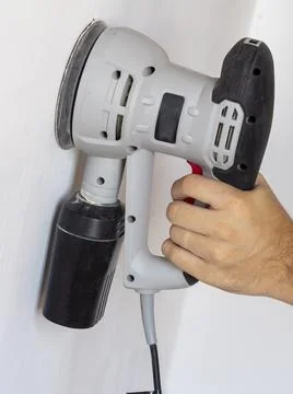 A Builder uses a sander to process a white concrete wall. Construction concer Foto stock