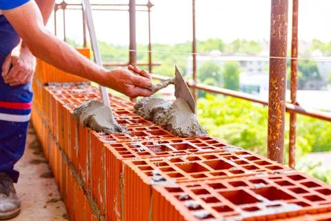Builder using spatula to set up mortar over red brick, building site Fotos de archivo