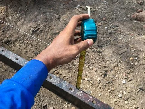 Builder is using a tape measure to find the distance between the ground and.. Stock Photos