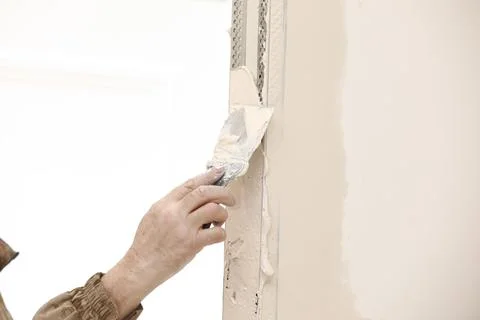 Builder using a trowel to add plaster. Plastering wall with putty-knife, close Stock Photos