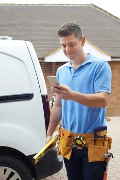 Builder With Van Checking Text Messages On Mobile Phone Outside House Foto stock