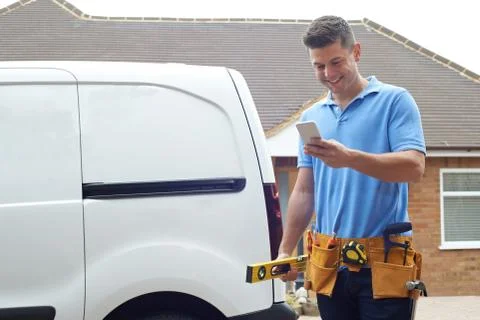 Builder With Van Checking Text Messages On Mobile Phone Outside House Stock Photos