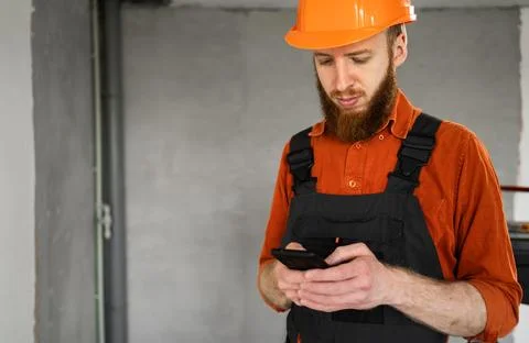 Builder wearing hard hat using a mobile phone standing at construction site Stock Photos