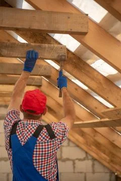 Builder in work clothes and gloves installing wooden roof truss beams with .. Stock Photos