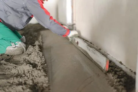 A builder in work clothes is doing his job, leveling the floor, pouring morta Stock Photos