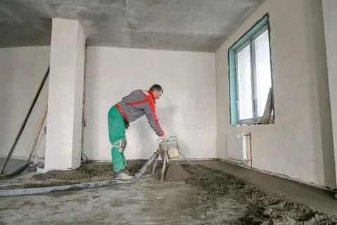 A builder in work clothes is doing his job, leveling the floor, pouring morta Stock Photos