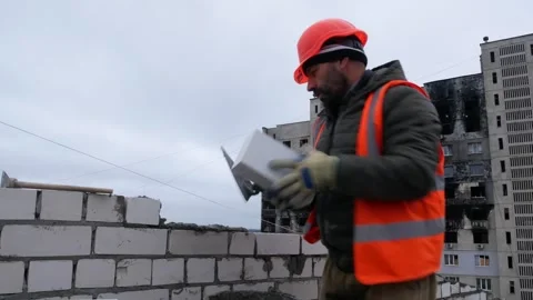 A builder in work clothes puts bricks on concrete and builds a wall. Stock Footage 317750466
