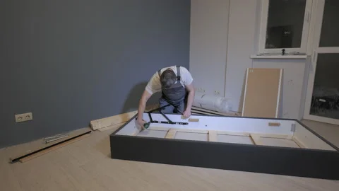 A builder in a work overalls is assembling a bed in a new apartment Stock Footage 170045226