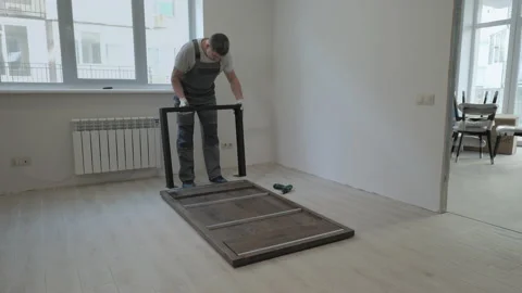 A builder in a work overalls is assembling a table in a new apartment Stock Footage 169872258