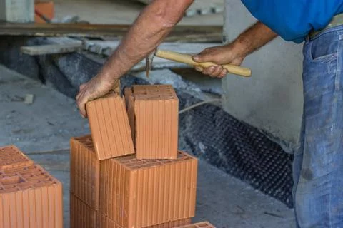 Builder worker cutting a clay block with brick hammer Stock Photos