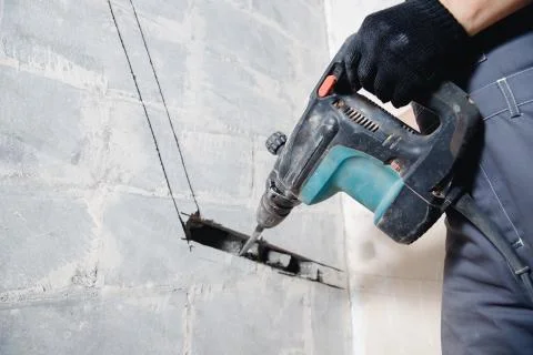 Builder worker man with hammer drill perforator equipment making hole in gray 스톡 사진