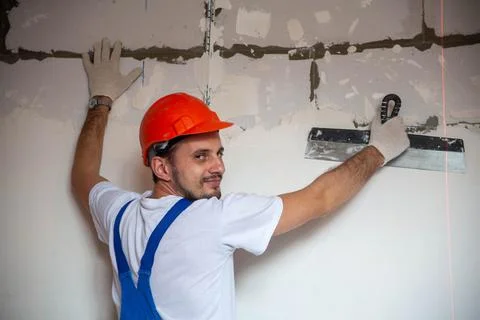 Builder worker plastering facade of high-rise building with putty knife Stock Photos