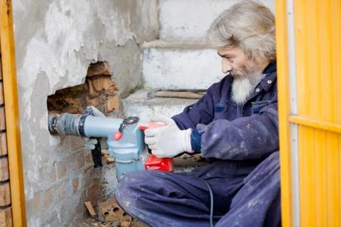 Builder worker with pneumatic hammer drill equipment breaking brick wall Stock Photos