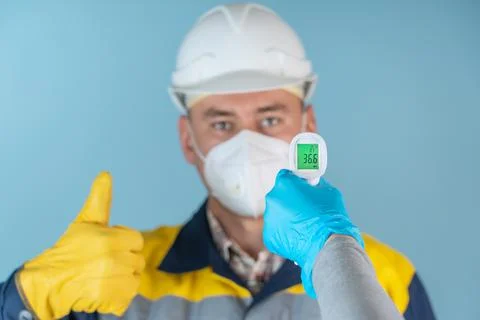 A builder, a worker in a protective face mask and a helmet have their tempera Stock Photos