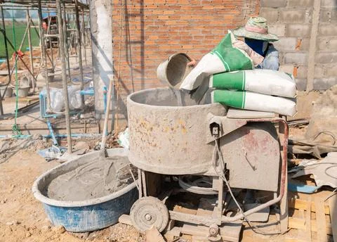 Builder working with a bucket in his hands loads a concrete mixer.orange co.. Stock Photos