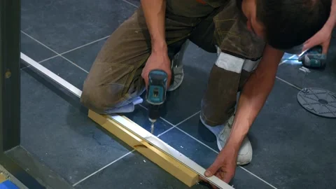 A builder in working form drills holes with a screwdriver into a white bar Stock Footage 154276572