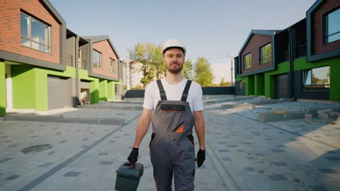 A builder in workwear and a hard hat carries a toolbox while walking near a Stock Footage 293637119