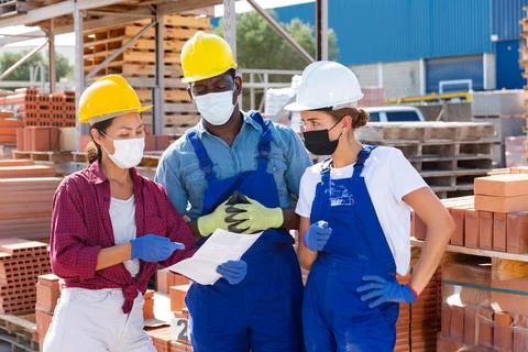 Builders and taskmaster in masks having conversation in warehouse Stock Photos
