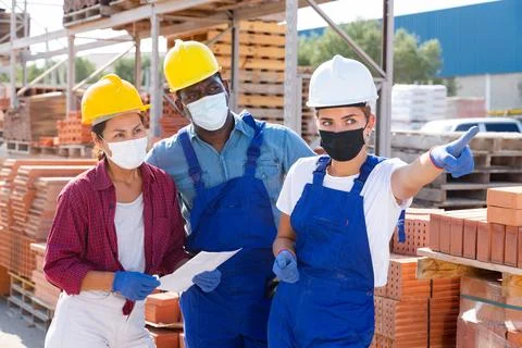Builders and taskmaster in masks having conversation in warehouse Stock Photos