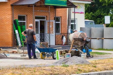 Builders are kneading a concrete solution with a concrete mixer. Stock Photos