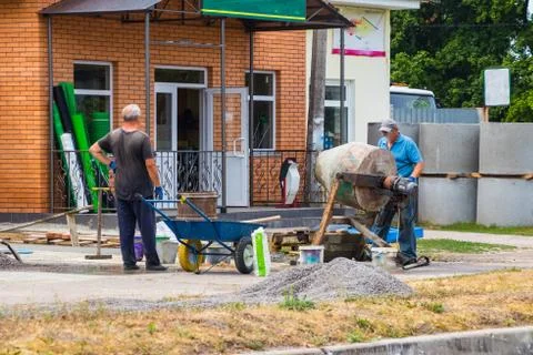 Builders are kneading a concrete solution with a concrete mixer. Stock Photos