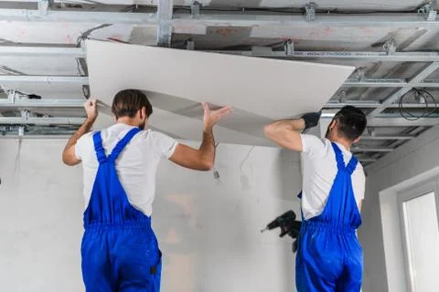 Builders in blue overalls making ceiling in apartment room Stock Photos