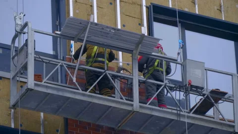A builders in a cradle on cables fastens decorative cladding panels on the wall  Stock Footage 229824495