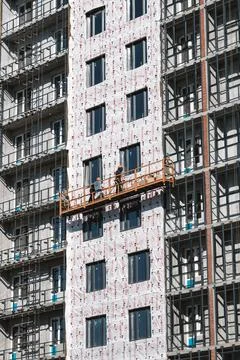 Builders on an industrial elevator are engaged in cladding and insulation of Stock Photos