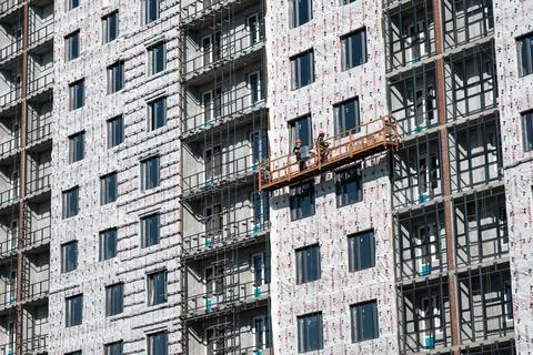 Builders on an industrial elevator are engaged in cladding and insulation of Stock Photos