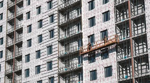 Builders on an industrial elevator are engaged in cladding and insulation of Stock Photos