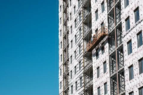 Builders on an industrial elevator are engaged in cladding and insulation of Stock Photos