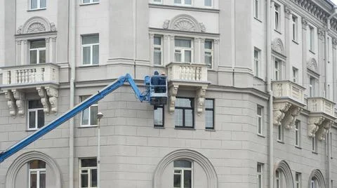 Builders on lifting boom platform standing near the building wall, constructi Stock Photos