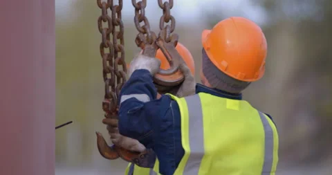Builders in orange helmets are about to lift a load with a crane and takes hooks Stock Footage 147633726