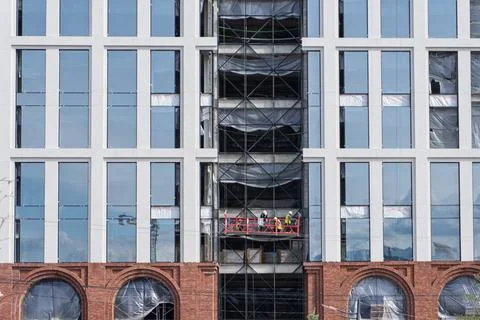 Builders on a suspended platform working on a modern glass building facade Stock Photos