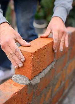 Building, construction and bricklayer with hands and cement, stacked bricks for Stock Photos
