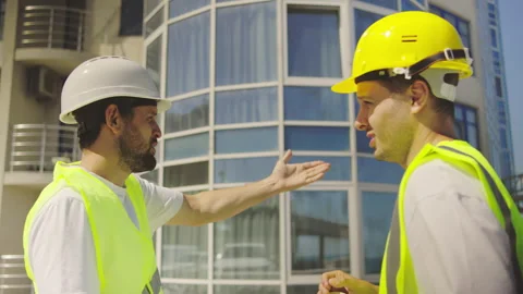 At a building construction site, an engineer in a white helmet discusses the Stock Footage 348242887