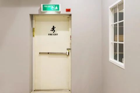 Building emergency exit with exit sign on door and fire extinguisher on the.. Stock Photos