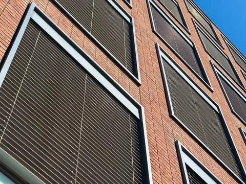 Building facade shows multiple windows with blinds during bright daytime Stock Photos