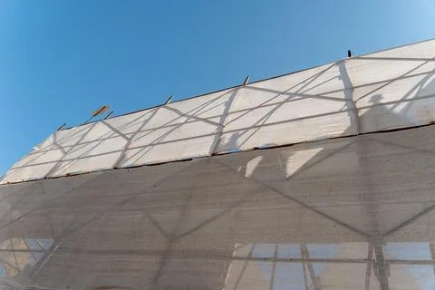 Building facade wrapped in white protective netting over scaffolding with Stock Photos
