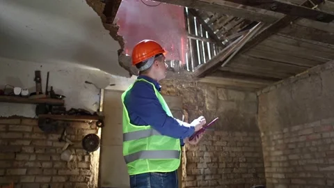 Building inspector. Man in a hard hat and a yellow reflective vest examines dama Stock Footage 205552014