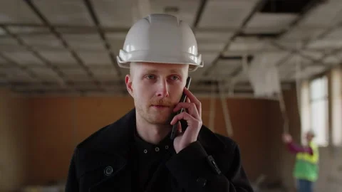 A building inspector is talking on the phone. A man in a white helmet reports Stock Footage 236644080
